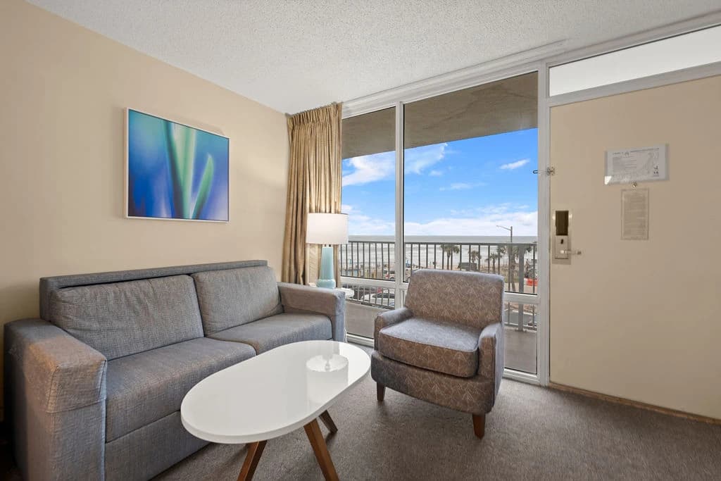 Studio living area with sofa bed, armchair, coffee table, and sliding door to balcony.