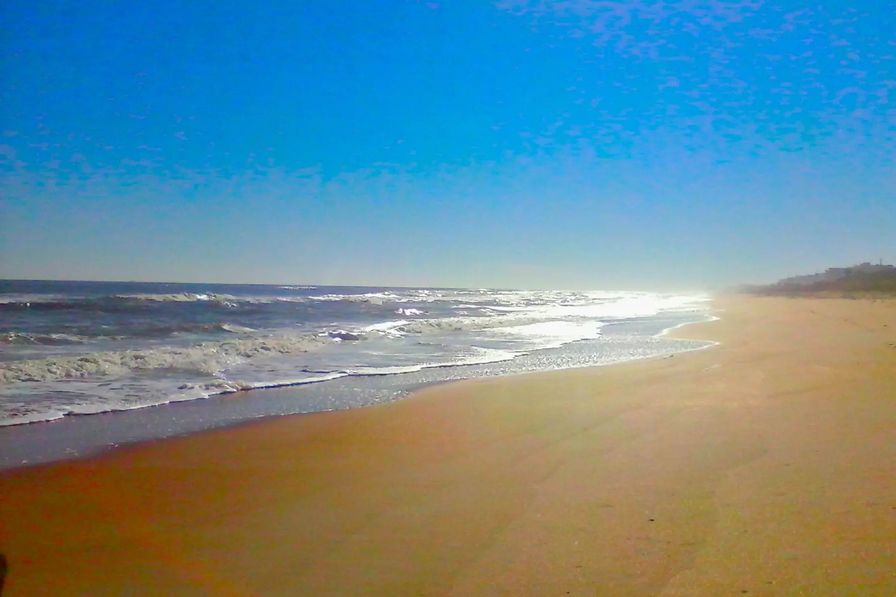Sandy beach shoreline with rolling waves under a clear blue sky.