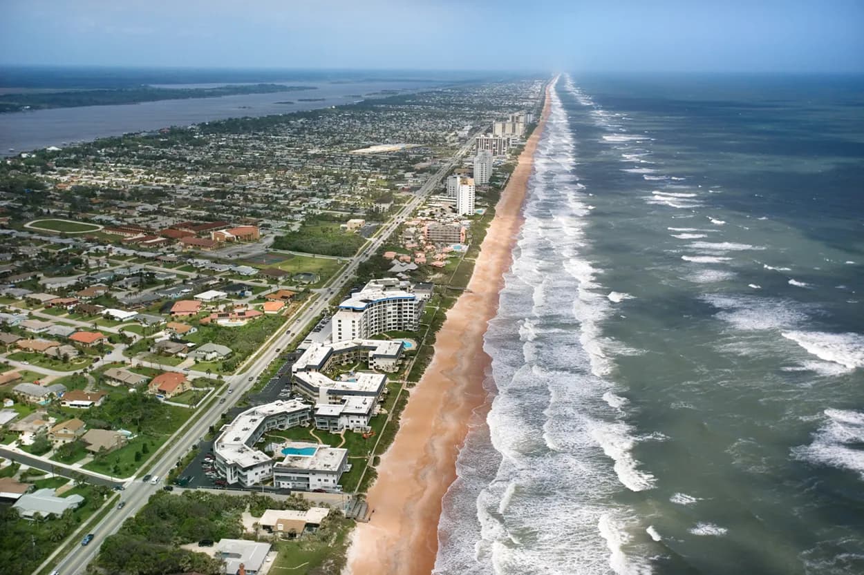 Aerial view of a long ocean coastline with beachfront buildings and residential neighborhoods.