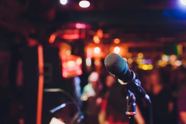Microphone on a stand in a dimly lit venue with colorful stage lights in the background.